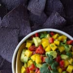mango avocado salsa in a white dish on a tray with purple corn chips