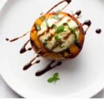 Half a grilled peach on a plate with orange ricotta & fresh basil on top. Drizzled with balsamic glaze (Top view)