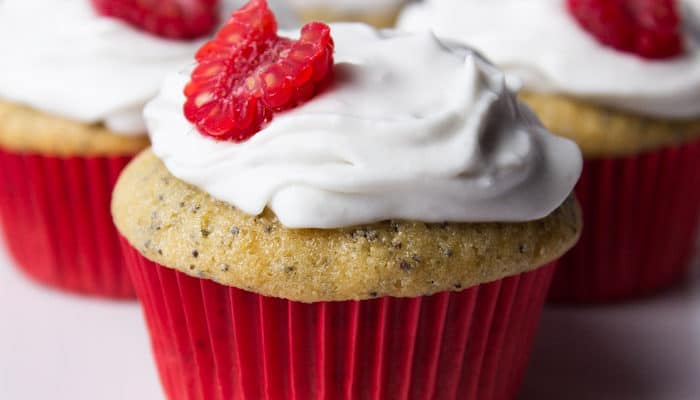 Close up of a poppyseed cupcake with a red paper topped with white frosting and half a raspberry