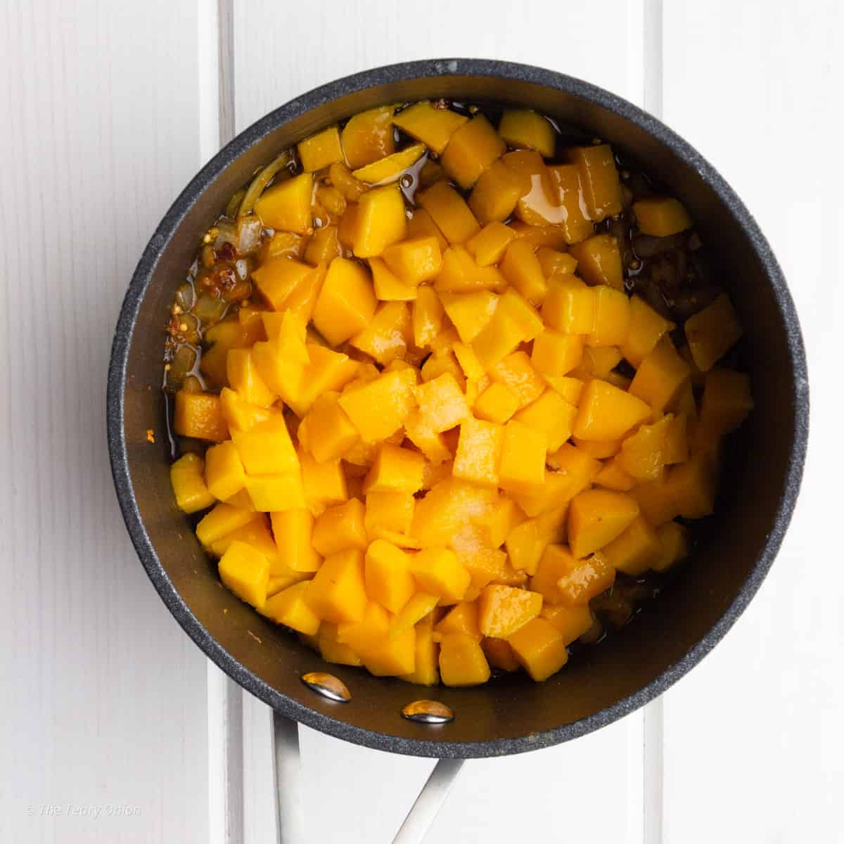 Diced mango in a small saucepan with sautéed onions and spices.