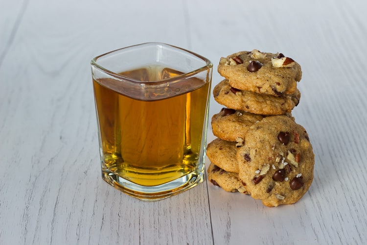 a stack of cookies next to a shot glass of bourbon