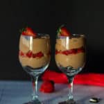 two wine glasses layered with crushed oreos, chocolate mousse, fresh strawberries and more mousse
