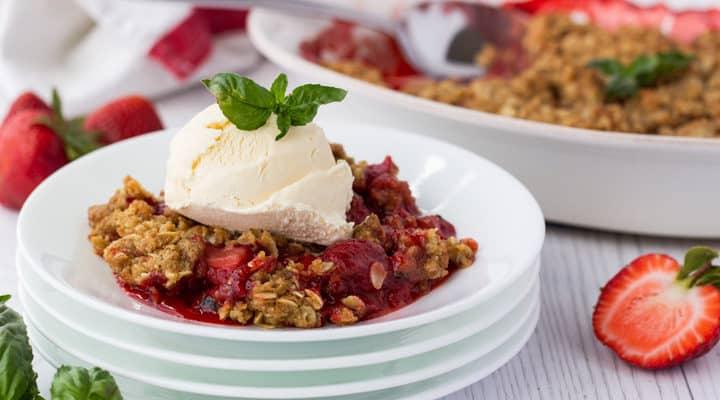a serving of strawberry basil crisp on a plate with ice cream on top. The pan of crisp is in the background.