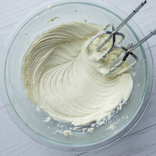 Beating vanilla and almond extract into sugar and cream cheese.