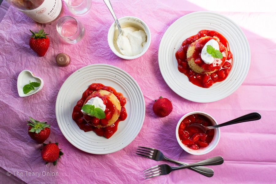 top view of two cakes on white plates with strawberry sauce and whipped cream