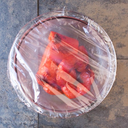 roasted red peppers in a clear glass bowl covered with plastic