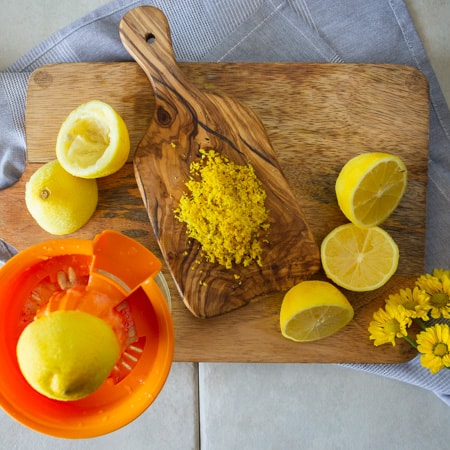 lemon halves on a wooded cutting board with a pile of lemon zest on a smaller cutting board