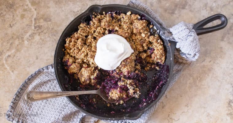 finished triple berry crisp with a dollop of whipped cream on top and a serving taken out. The spoon sitting in the pan
