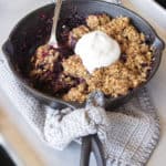 triple berry crisp with a dollop of whipped cream on top and a serving taken out. The spoon sitting in the pan