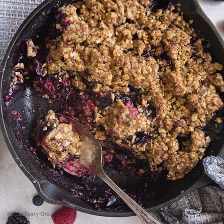 finished triple berry crisp with a serving taken out and a spoon sitting in the pan