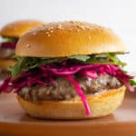 A gourmet burger with pickled cabbage and arugula on a brown plate
