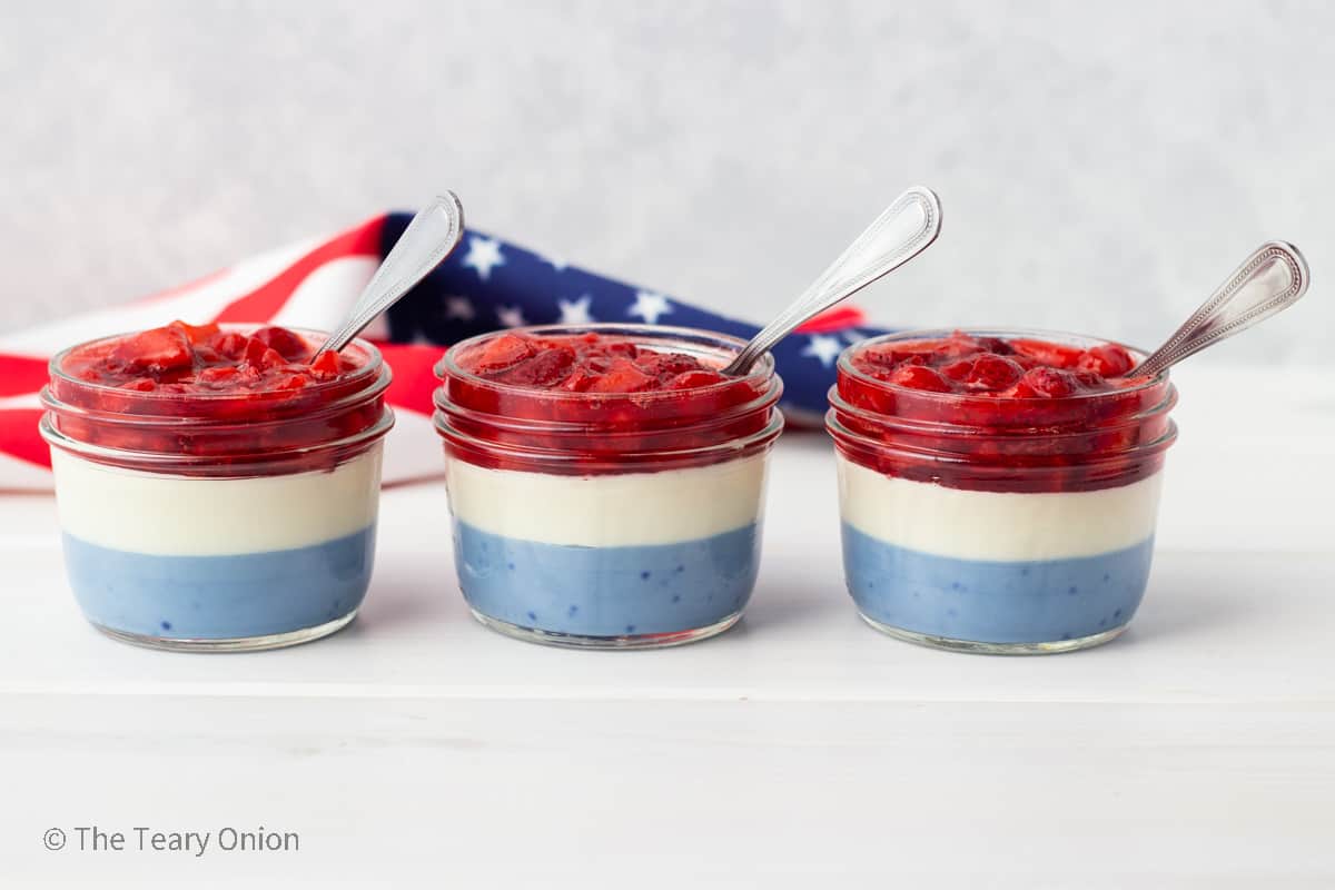3 mason jars with a blue and white mousse layer and a red strawberry layer.