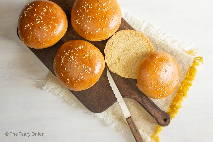 whole wheat hamburger buns on a cutting board with one cut in half