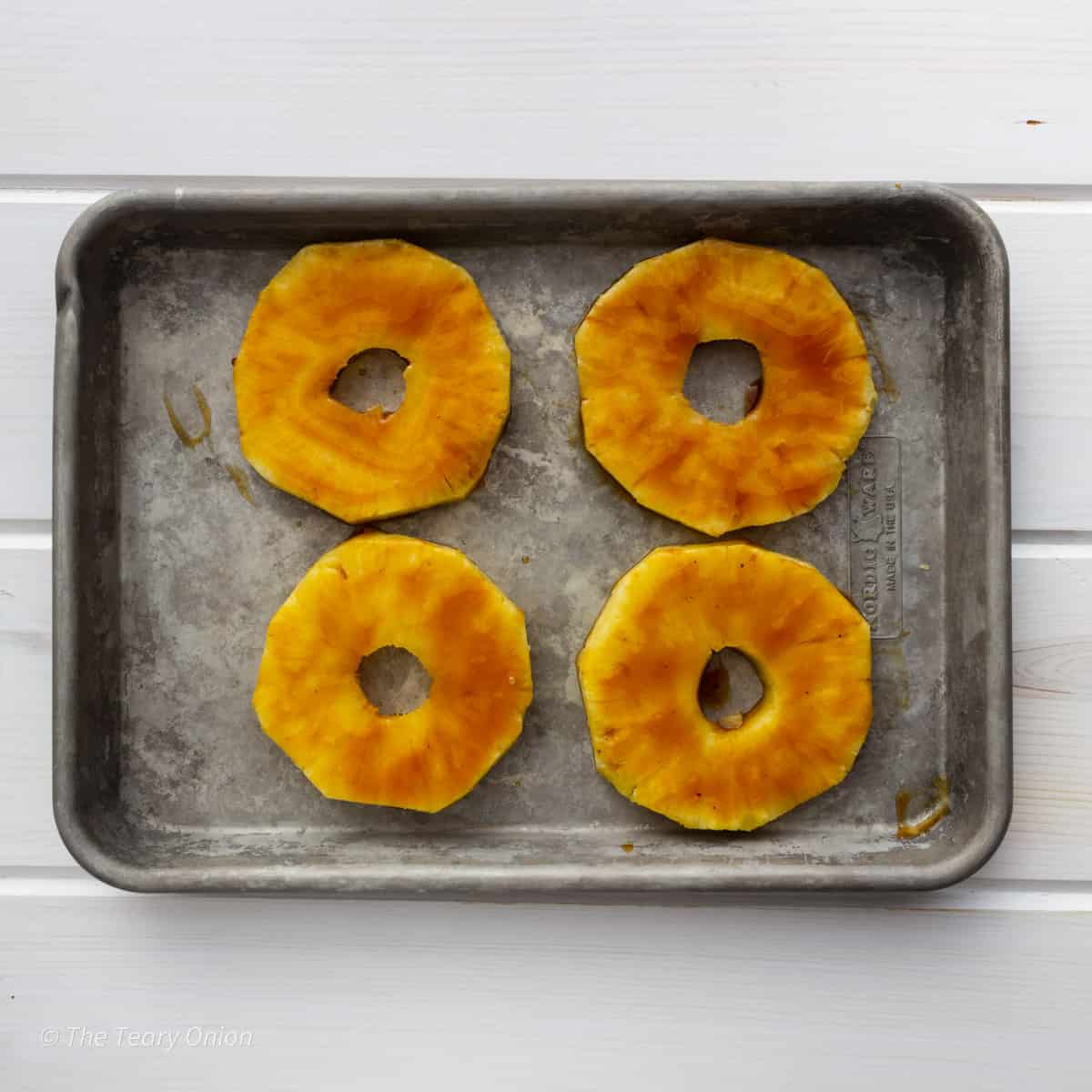 4 fresh pineapple rings on a tray brushed with teriyaki sauce.