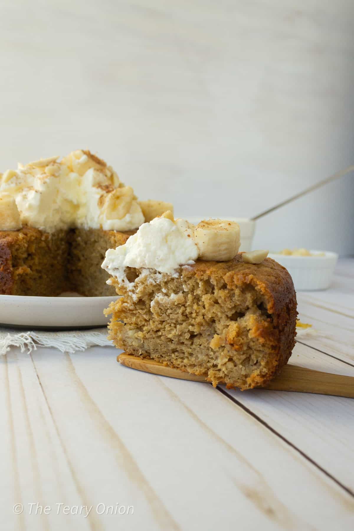 A slice of healthy banana cake with whipped cream, fresh bananas and slivered almonds on top.